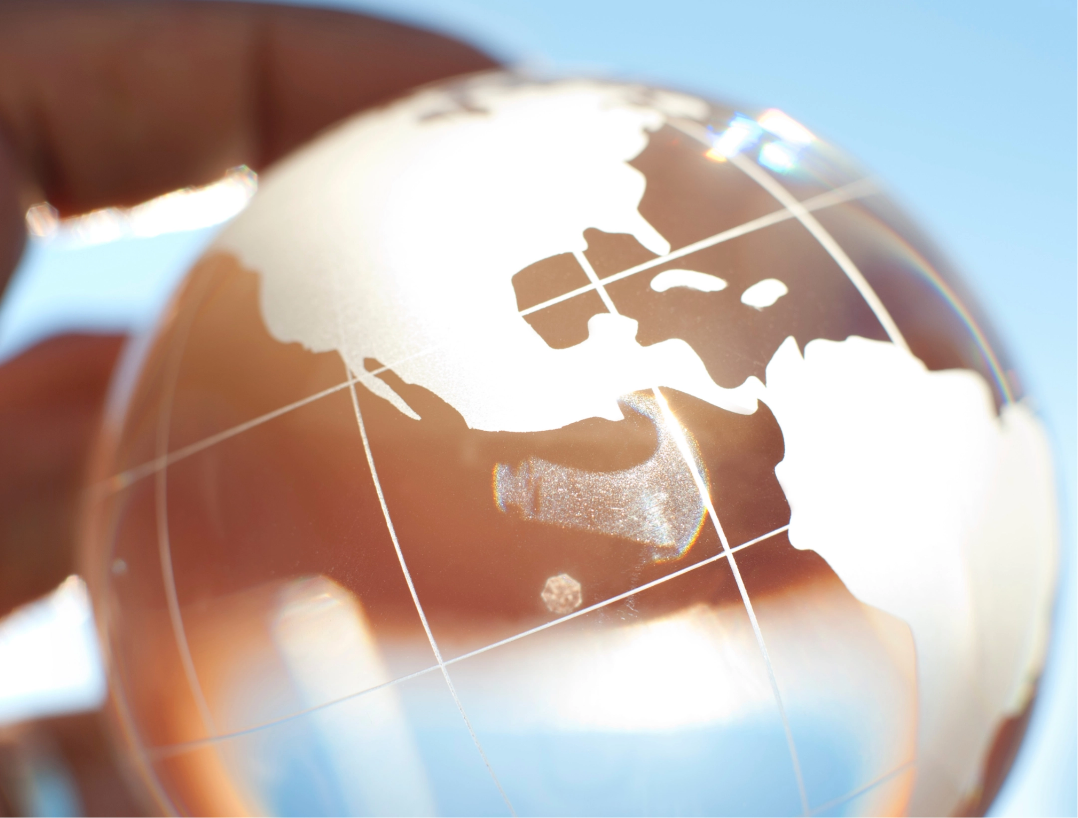 Close-up of a transparent glass globe showing etched world map against a blue sky