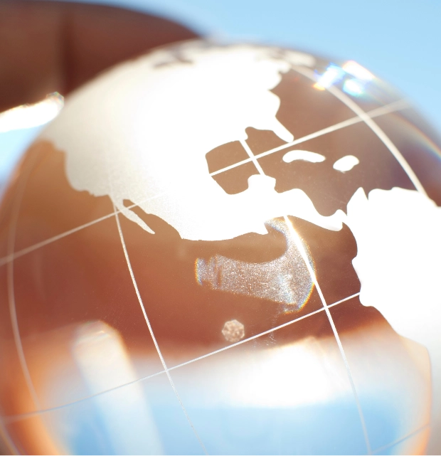 Close-up of a transparent glass globe showing etched world map against a blue sky